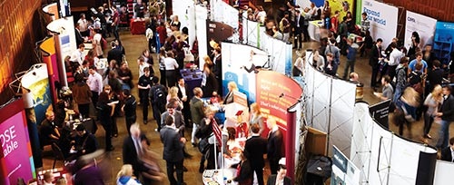 A crowd of people walking around exhibition stands at a careers event